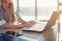 Woman blogging in spacious office using computer on her workplace. Female employee sitting, smiling, looking at camera.