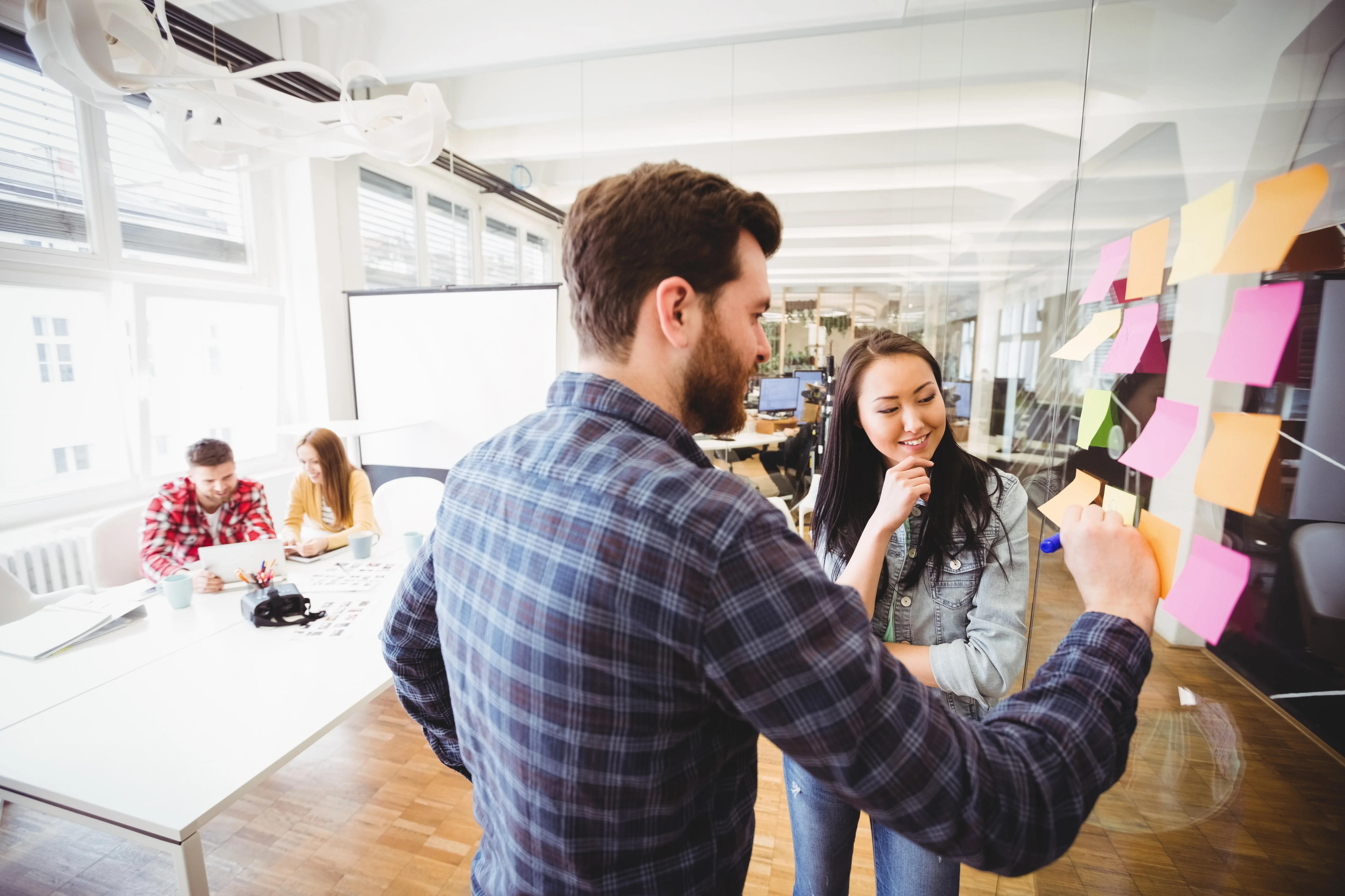 Businesswoman looking coworker writing on sticky notes So arbeitet die Digitalagentur der Zukunft