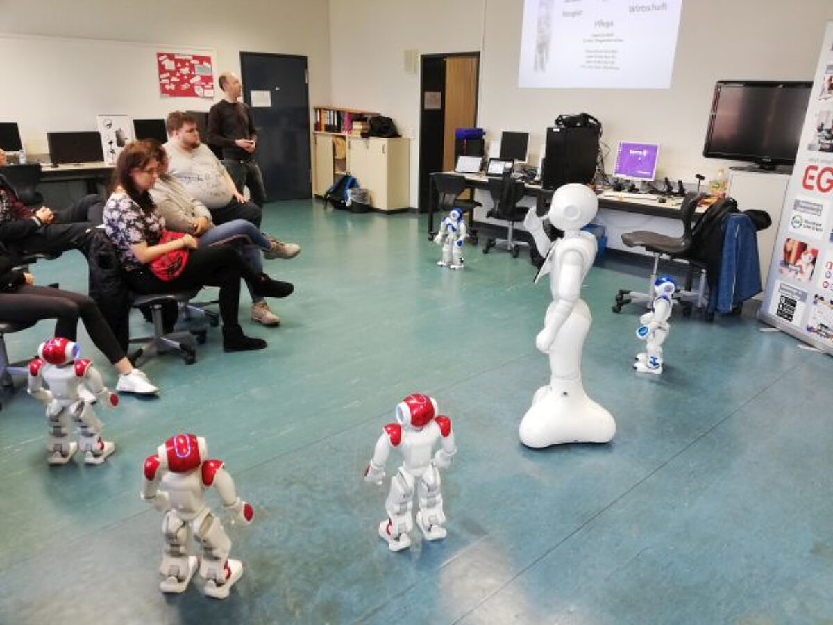Ein Pepper-Roboter, umringt von mehreren Nao-Robotern, stellt sich vor. Ein Pepper-Roboter, umringt von mehreren Nao-Robotern.