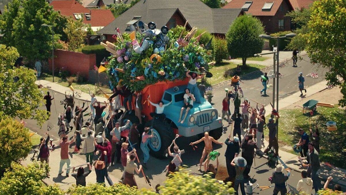 Markenrelevanz: Menschen feiern auf der Straße um einen riesigen LKW, der mit Pflanzen, Werkzeugen und Gartenzubehör überladen ist.