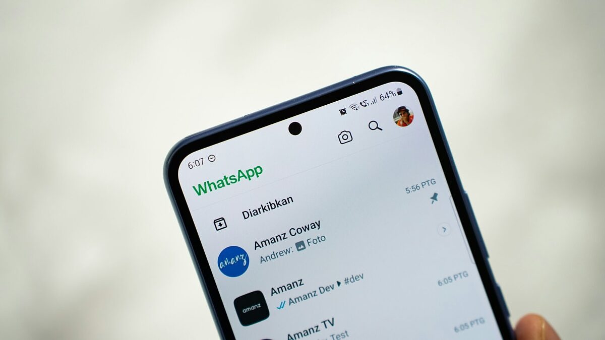 A person holding a cell phone showing WhatsApp chats on the screen.
